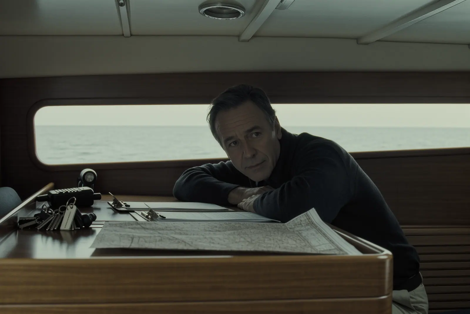 The chart table below deck during a charter briefing: paperwork and a clipboard beside a folded paper chart, keys with a plain tag, a handheld VHF and a torch.