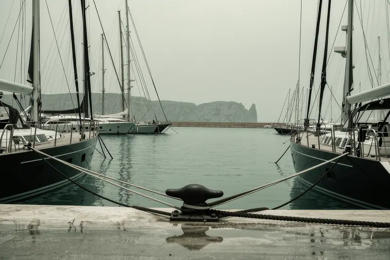 Charter yachts moored stern-to along a working quay in Palma, mooring lines and a cast-iron cleat in the foreground, masts crowded along the wall.