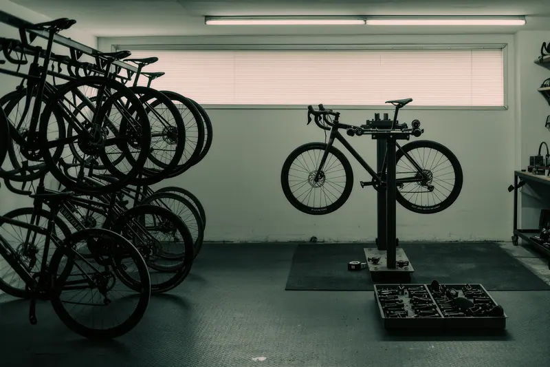 The inside of a bike rental workshop with bikes in a wheel rack, a repair stand and a bench of tools and small parts.